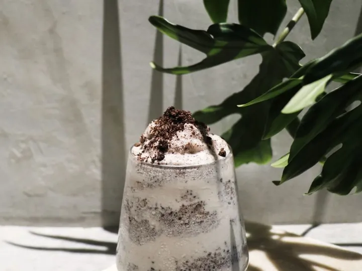 Cookies and cream milkshake topped with cream and Oreo crumbs on a marble coaster