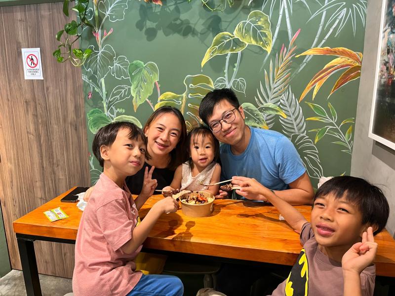 A family sharing açaí bowls at a wooden table in front of the tropical mural inside Olá Açaí