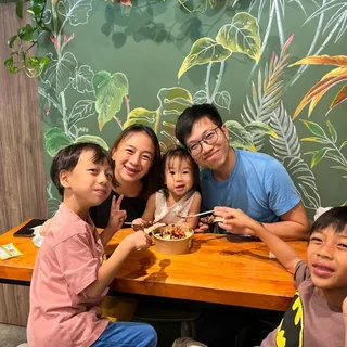 A family sharing açaí bowls at a wooden table in front of the tropical mural inside our shop