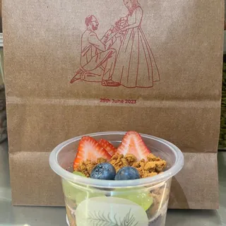 Takeaway açaí cup topped with strawberry and blueberry, with our branded paper bag